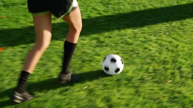 A soccer player running with a football dribbling up the grass field to score a goal and win the game.