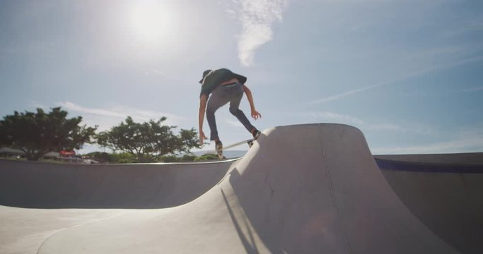 Skateboarder skateboarding in slow motion jumping out of a concrete bowl and over the over side, professional skateboarding tricks in slow motion