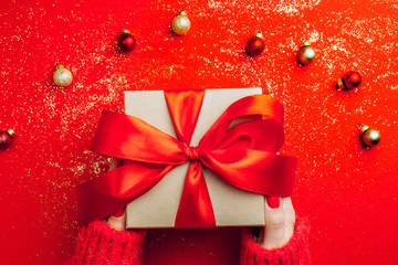 Female hands holding present with red bow on red sparkling background. Festive backdrop for...