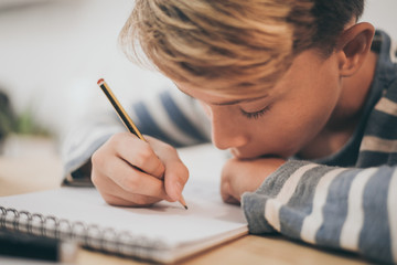 Student drawing with pencil on the notebook. Boy doing homework writing on a paper. Kid hold a...