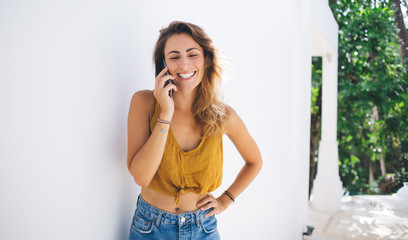 Fototapeta premium Cheerful modern fit young woman in casual outfit having phone call while standing on gray background