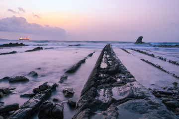 Big boat off the coast with strange rocky shapes at sunset.