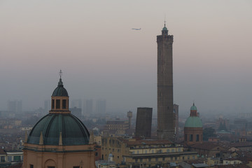 An airplane flies over Bologna at sunset in a foggy Bologna