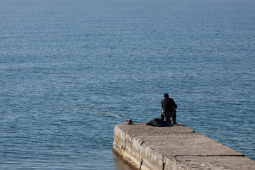 Fototapeta na wymiar Fisherman fishes in the sea from the pier
