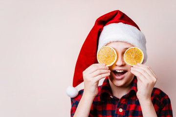 christmas time. funny cute boy in santa hat closing eyes with dried orange slices. Holiday treats...