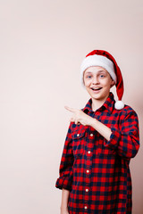 enthusiastic motivated overexcited boy wearing santa claus hat points with index finger at empty space, advertisement, banner or poster template, emotion facial expression, people reaction