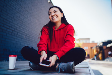 Takeaway cup with copy space area for advertising text, happy japanese female blogger with modern cellular gadget in hands feeling excited from generation time spending time on public place