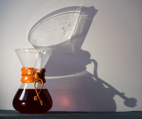 Glass container filled with black coffee on one-ton white background with reflection of large and unusual shadows.