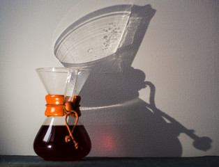 Glass container filled with black coffee on one-ton white background with reflection of large and unusual shadows.