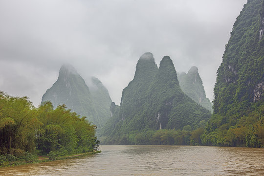 Steep hills bordering the Li River pointing to the clouds in the vicinity of Yangshuo near Guilin