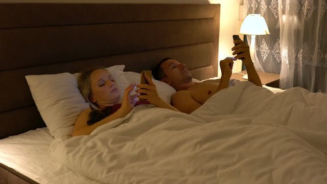couple lies in bed and use smartphones