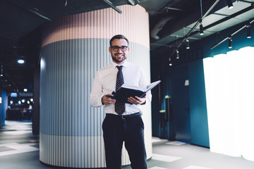 Portrait of man successful bookkeeper holding textbook with accounting information and smiling at...