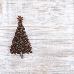 Shape of Christmas tree made of coffee beans, anise star and cinnamon sticks, on wooden table. Winter holidays concept. Top view, copy space. Wooden, natural background