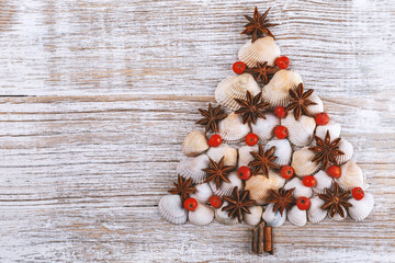 Christmas tree made from different type of sea shells, anise star, rowan berries and starfish with on wooden background. Sea shells shaped as a Christmas tree. New Year celebration concept, top view