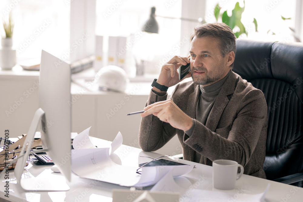 Poster Confident architect talking on the phone while pointing at computer screen