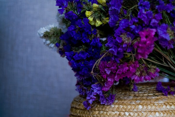 Bouquet of multicolored colors of dry flowers on one-ton background on woven hat made of straw. Violet.