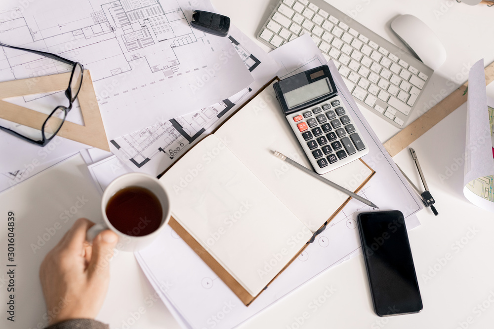 Aufkleber Overview of hand of engineer with cup of black tea or coffee by desk during work