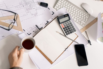 Overview of hand of engineer with cup of black tea or coffee by desk during work