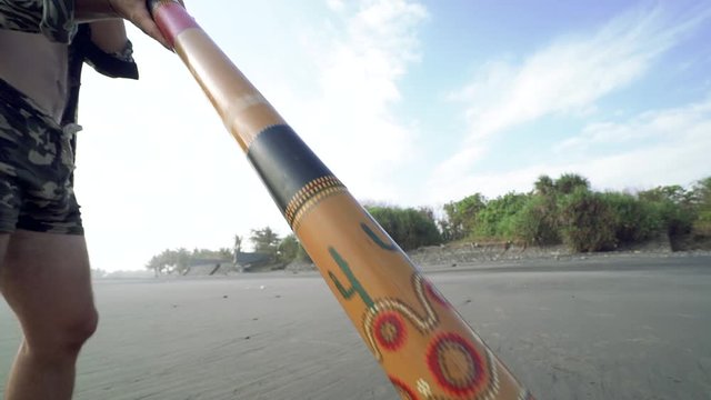 Young musician man playing on didgeridoo on beach at sunset.