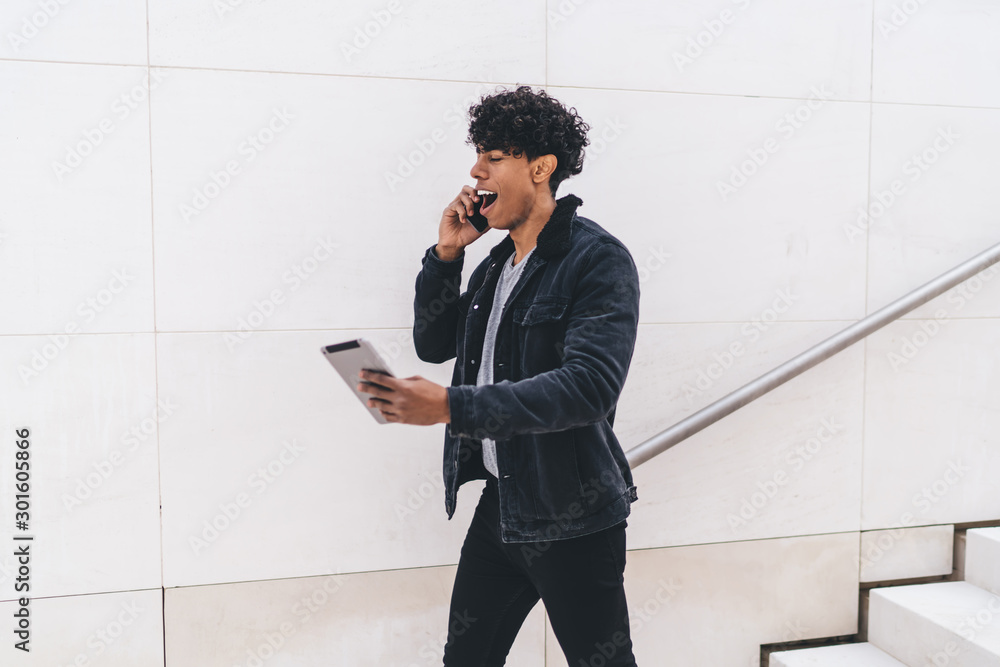 Poster Shocked Latino man checking received email with account balance while walking at urban setting and making smartphone call for discussing information, hipster guy amazed from touch pad notification