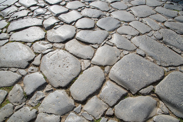 A fragment of the original cobblestone pavement of time-worn stones built by Ancient Rome. Background. Pattern. Gray.