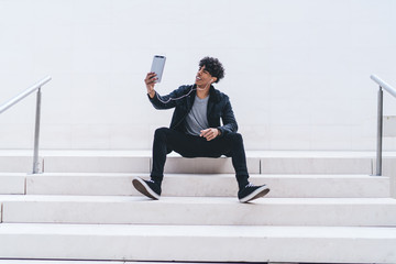Fototapeta premium Handsome hipster guy in stylish clothing resting at city stairs and shooting online video for sharing to social networks using 4g wireless internet connection for browsing websites, generation