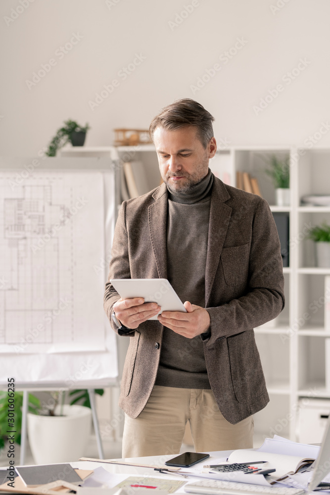 Poster Confident architect in formalwear scrolling in tablet while standing by desk