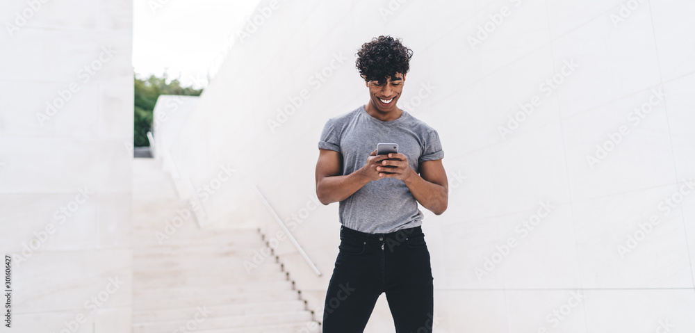 Poster smiling young man sending message on smartphone standing at city urban setting with public wifi, pos