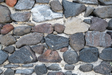 A fragment of an old stone wall made of rough stones. Background. Gray.