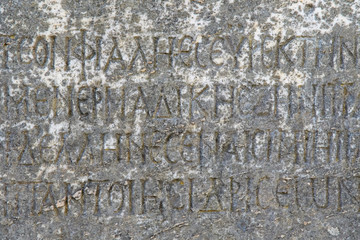 Half-erased ancient Greek letters embossed on an old gray marble slab covered with cracks and mold.