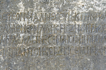 Half-erased ancient Greek letters embossed on an old gray marble slab covered with cracks and mold.