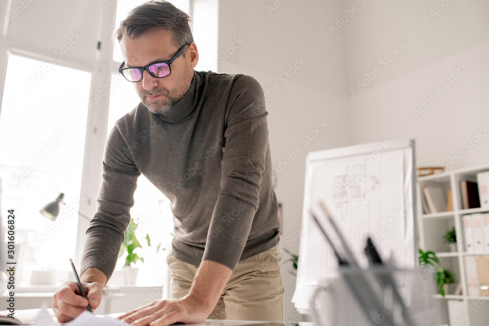 Poster Confident engineer bending over papers while drawing new sketches in office