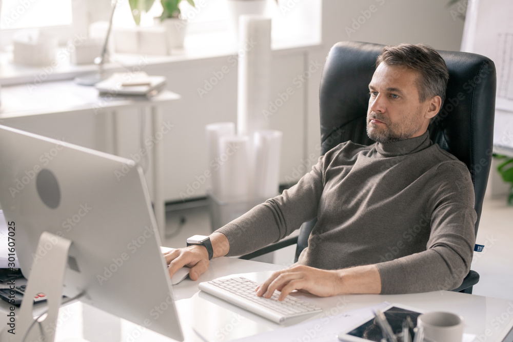 Poster Serious manager concentrating on work while sitting in front of computer screen