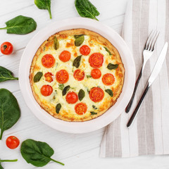Quiche pie with spinach, cherry and mozzarella. Cutlery on a napkin. The concept of delicious food, recipes, bakery.