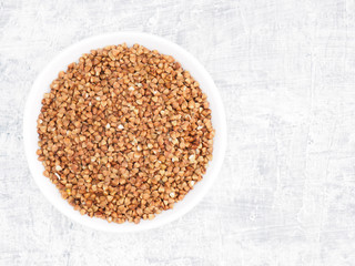 Buckwheat groats in a ceramic bowl on a white cement background. Healthy eating concept