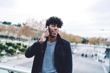 Happy Latino male tourist using public internet for making online call via cellphone application...