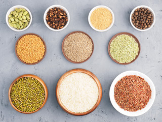 White rice, brown rice, mung bean, green cardamom, allspice, cumin, fenugreek, cloves, masala, fennel on gray concrete background. Indian cuisine, ayurveda, naturopathy concept