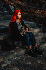 Fototapeta premium Sexy redhead girl with long hair plays the ukulele. Perfect woman portrait. Gorgeous strong and thick hair. Deep blue eyes. Natural beauty, clean skin, face and hair care.