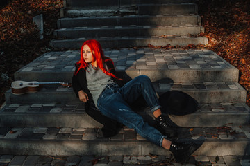 Sexy beautiful redhead girl with magnificent long hair. Ukulele playing, sitting on the steps in...