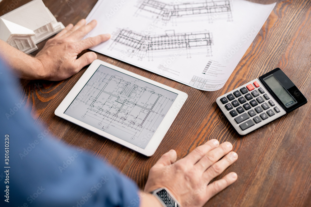 Poster hands of modern engineer leaning on wooden table while bending over tablet
