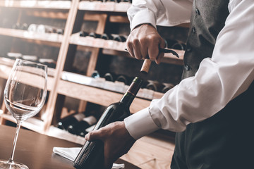 Sommelier Concept. Senior man standing opening wine bottle holding corkscrew close-up