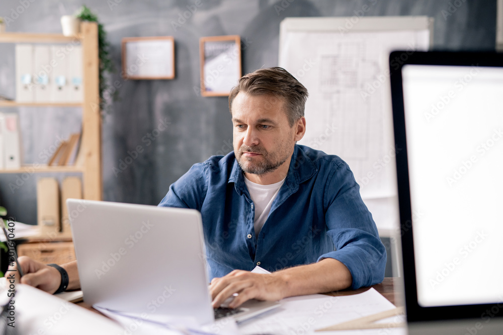 Poster Architect sitting in front of laptop, looking through data and making sketch