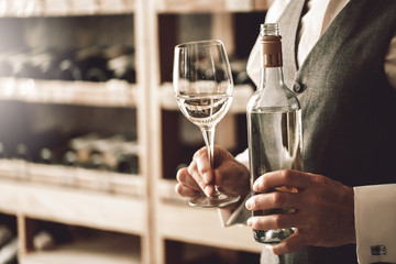 Sommelier Concept. Senior man standing with bottle and glass of white wine close-up