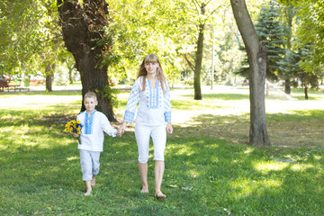 Naklejka na ściany i meble mother and son in embroidered shirts walk barefoot on the grass. national clothes of Ukraine.