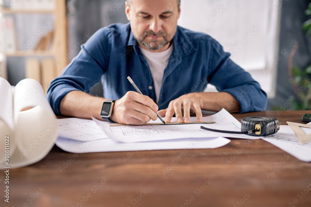 Poster Bearded mature engineer using pencil and ruler while drawing line on sketch