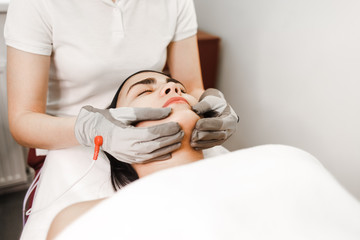 Microcurrent therapy. Cosmelotologist makes stimulating facial massage with electric gloves. ...