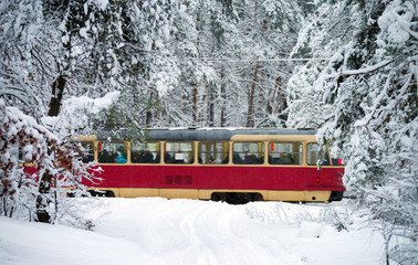 Red yellow tram rides through the snowy forest. In move. Selective focus.