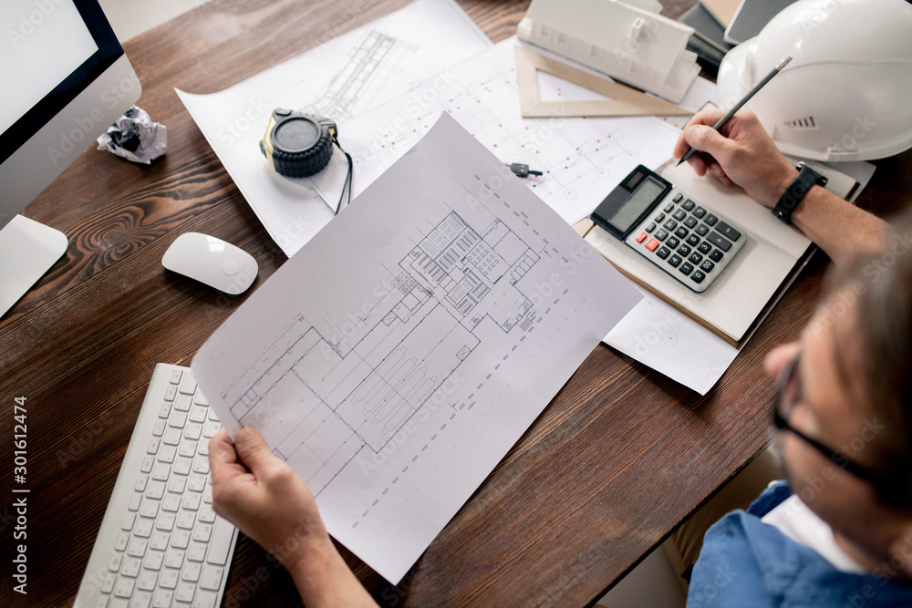 Poster Paper with sketch held by engineer looking at blueprint and making notes