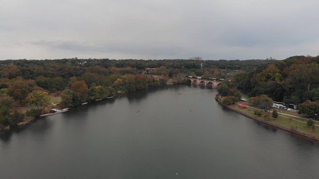 Cinematic aerial view of a peaceful river, railroad bridge with arches and a train crossing in a beautiful autumn landscape. Fall foliage in rural Pennsylvania. Rowing and crew teams on a river.