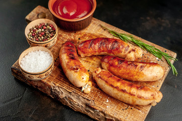 Grilled sausages with spices, ketchup and rosemary on a stone table, ready to eat